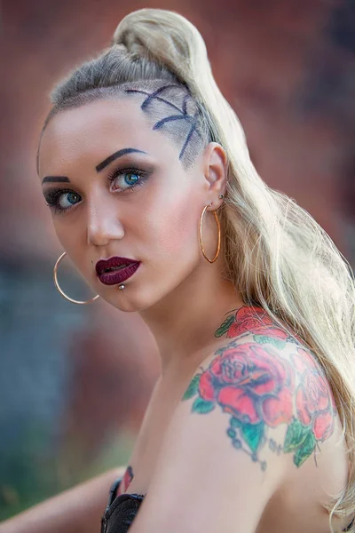 blonde girl with tattoos in leather corset on brick wall background, close up