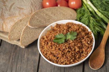 Bir kase maydanoz bir delikanlı ile karabuğday lapası, bir bardak süt ve domates koyu bir kaba ahşap masada. geleneksel Rus yemeği. Rustik tarzda. Boşluk Kopyala. dereotu, soğan, yeşillikler, üst görünüm