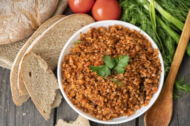 Bir kase maydanoz bir delikanlı ile karabuğday lapası, bir bardak süt ve domates koyu bir kaba ahşap masada. geleneksel Rus yemeği. Rustik tarzda. Boşluk Kopyala. dereotu, soğan, yeşillikler, üst görünüm