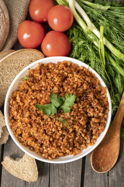 Bir kase maydanoz bir delikanlı ile karabuğday lapası, bir bardak süt ve domates koyu bir kaba ahşap masada. geleneksel Rus yemeği. Rustik tarzda. Boşluk Kopyala. dereotu, soğan, yeşillikler, üst görünüm