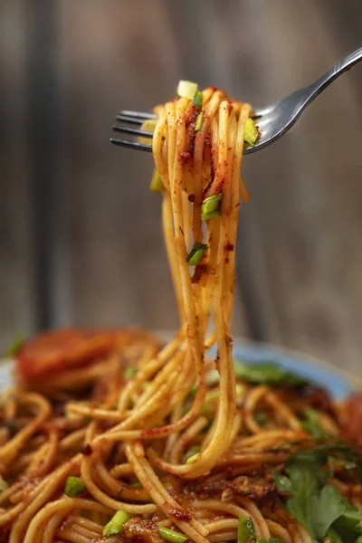 plate of pasta seasoned with herbs, tomatoes and sauce on a wooden table close-up, fork with long pasta and sauce, share menu restaurant and cafe