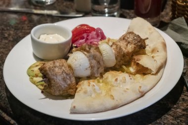 Beyaz plaka yakın çekim üzerinde düz ekmek ve sebze ile ahşap şiş üzerinde et kebap