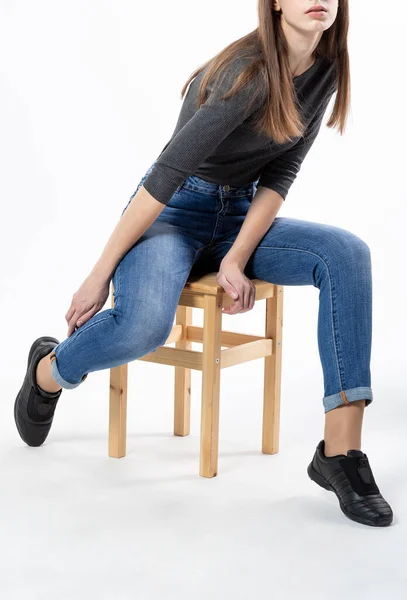 穿着牛仔裤的女孩坐在木制长椅上 穿着白色背景的紧身牛仔裤 蓝色牛仔裤 — 图库照片