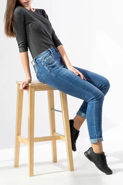 穿着牛仔裤的女孩坐在木制长椅上 穿着白色背景的紧身牛仔裤 蓝色牛仔裤 — 图库照片