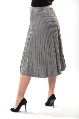 Beyaz arka planda uzun dalgalı etekli, ince bacaklı, güzel bir kız. Uzun, gri, dalgalı etekli, yakın plan.