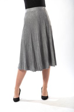 Beyaz arka planda uzun dalgalı etekli, ince bacaklı, güzel bir kız. Uzun, gri, dalgalı etekli, yakın plan.