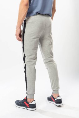 Beyaz arka planda eşofmanlı ve spor ayakkabılı atletik bir adam.