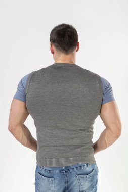 Örgü bir yelek ve beyaz arka planda mavi kot giyen bir adam.