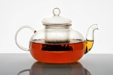 Beyaz zemin üzerinde sıcak çay ve yansımalı cam çaydanlık.