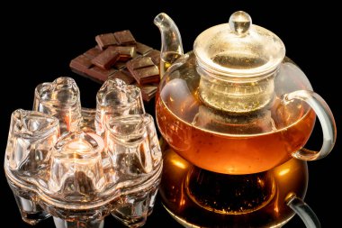 Cam tezgahlı cam çaydanlık, siyah zemin üzerinde bir mum, cam çaydanlıkta siyah çay, çikolatalı çay ile ısıtılır.