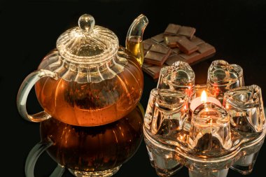 Cam tezgahlı cam çaydanlık, siyah zemin üzerinde bir mum, cam çaydanlıkta siyah çay, çikolatalı çay ile ısıtılır.