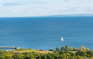 Deniz kıyısında beyaz yelkenli yelkenli bir yatın manzarası.