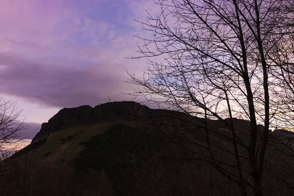 Silhouette of Arthur Seat seen at dawn against purple sky in Edinburgh, Scotland.