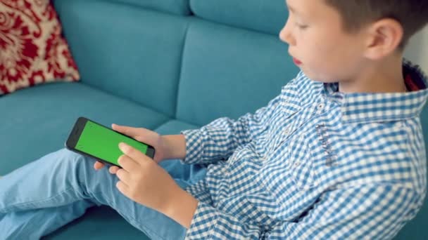 The child is holding a phone in his hand with a green screen — Stock Video