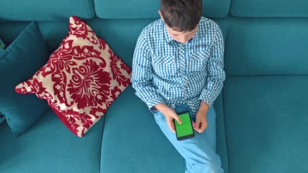El niño sostiene un teléfono en la mano con una pantalla verde — Vídeos de Stock