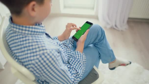 A criança está segurando um telefone na mão com uma tela verde — Vídeo de Stock