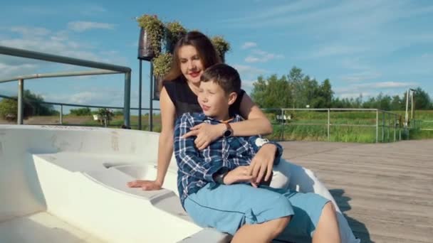 Moeder en zoon zitten op een witte boot op een houten pier en genieten van het platteland. — Stockvideo