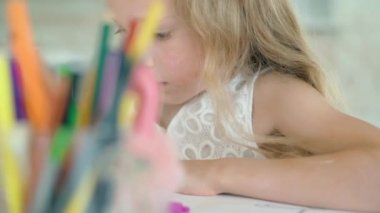 Sevimli küçük kız masada oturur ve kalemler ile çizer.