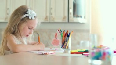 Sevimli küçük kız masada oturur ve kalemler ile çizer.