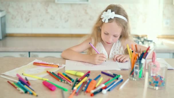 Una niña linda se sienta en su escritorio y dibuja con lápices — Vídeos de Stock
