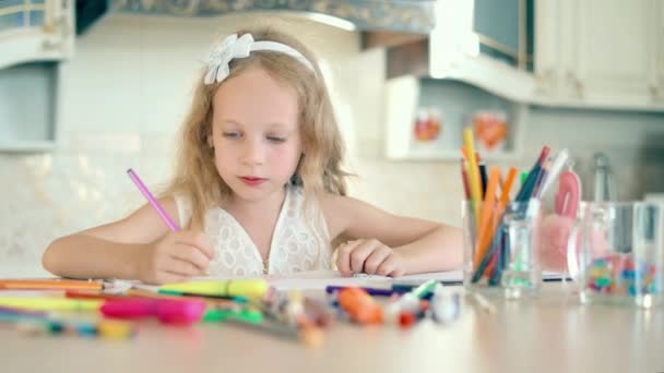 Una niña linda se sienta en su escritorio y dibuja con lápices — Vídeos de Stock