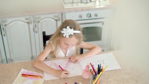 Linda niña se sienta a la mesa y dibuja con lápices . — Vídeos de Stock