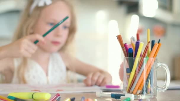 Schattig klein meisje zit aan de tafel en tekent met potloden. — Stockvideo