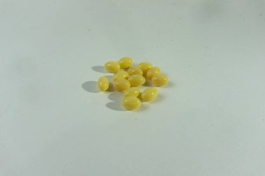 Küçük, dikdörtgen, sarı jelatin kapsüller temiz ve şeffaf bir arkaplanda bulunur. Bu softgel hapları, genellikle ilaveler ve ilaçlar için kullanılır, basit ve düzensiz bir şekilde sunulur.