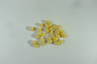 Küçük, dağınık, şeffaf sarı jelibon yığını temiz beyaz bir arka planda yatıyor. Şekerler oval şekillidir ve hafif bir kaynaktan dökülen ince gölgelere sahiptir.