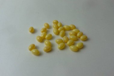 Küçük, oval, sarı jelatin kapsüller ya da haplardan oluşan bir koleksiyon temiz, beyaz ve şeffaf bir arkaplana saçılmıştır. Softgeller bir stüdyo çekiminde gösterilir, onların basit, parlak