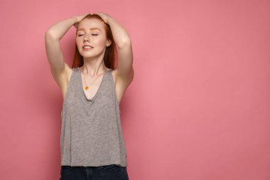 Genç kızıl saçlı kadın gözlerini kapayarak saçlarını düzeltiyor.