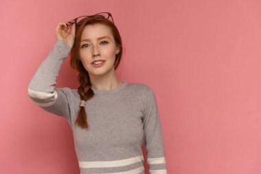 Örgülü kızıl saçlı kız kameraya gülümsüyor gözlük koyarak