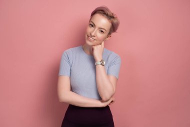 Pembe saçlı genç kadın başını eğerek kameraya bakıyor 