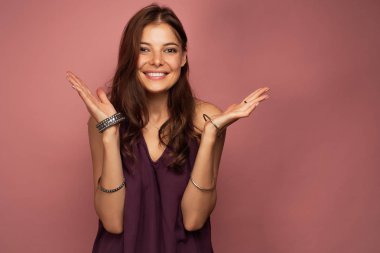 Genç esmer kamera, pembe arka planda gülümseyen bilezik ile ellerini yayılır
