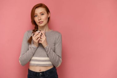 Redhead genç kadın bir fincan tutar ve pembe arka planda kamera bakıyor