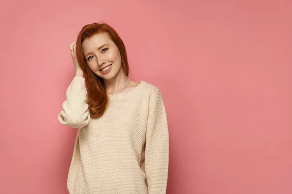 Redhead Girl berör hennes hår och ler på rosa bakgrund — Stockfoto