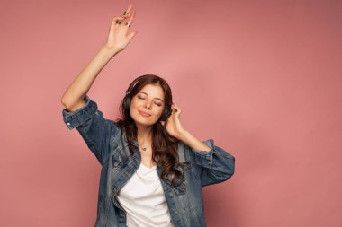 Gözleri kapalı, pembe arka plan ile onun kulaklıklar müzik zevk genç koyu saçlı kadın dansları