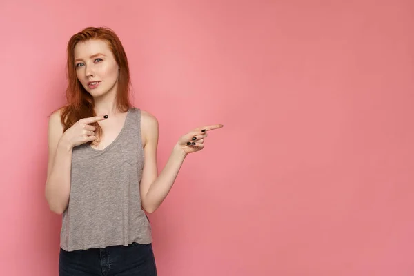 Redhead kvinna pekar fingrarna på tomt utrymme till höger om fotot tittar på kameran — Stockfoto