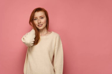 Redhead kız saçlarına dokunur ve pembe arka plan üzerinde gülümsüyor
