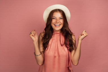 Şapka takan genç esmer, ellerini zevkle kenetleten kameraya gülümsüyor