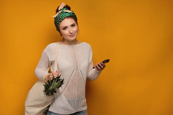 Fiatal nő egy ananász az ő bevásárlótáska jelent több mint sárga háttér — Stock Fotó