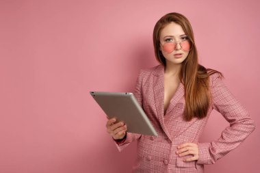 Genç kadın pembe arka plan üzerinde pembe gözlük ile düşünceli kameraya bakar