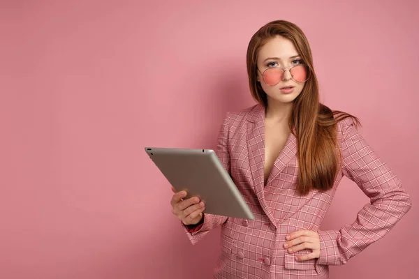 Молодая женщина задумчиво смотрит в камеру через розовые очки на розовом фоне — стоковое фото
