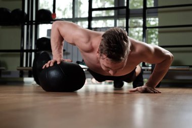 Çıplak gövdeli kaslı bir adam elini topun üzerinde titretecek şekilde barda duruyor..