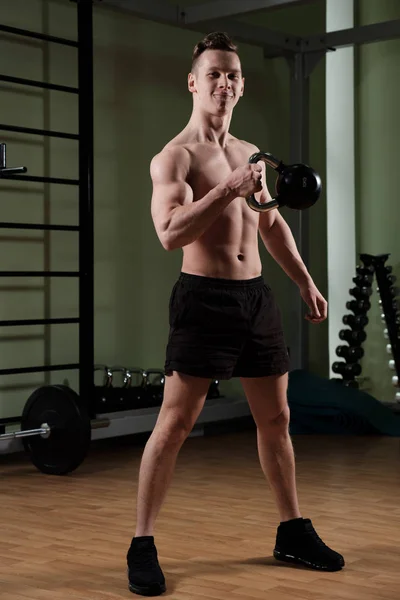 Un ragazzo muscoloso con un busto nudo in pantaloncini sportivi sta correndo su un kettlebell con una mano, labbra borsette divertenti . — Foto Stock