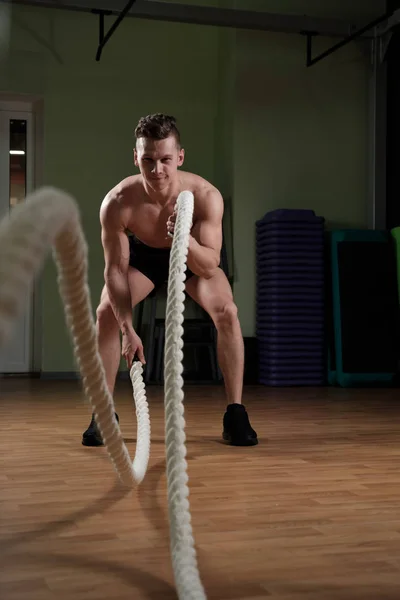 Atletismo hombre adulto con cuerda de batalla haciendo ejercicio iin gimnasio de entrenamiento funcional. — Foto de Stock