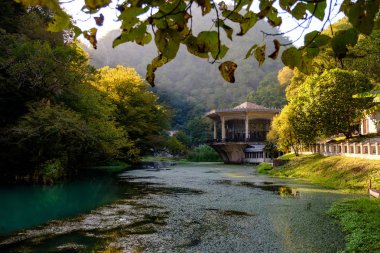 Yeşillikler arasında bir dağın eteklerinde bir gölün üzerinde eski terk edilmiş bir bina.
