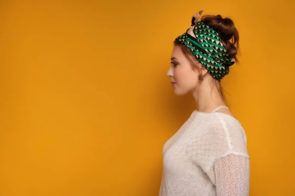Egy fiatal lány egy könnyű pulóvert, és egy fejkendő holtversenyben egy színes sálat áll profilja a sárga háttér. — Stock Fotó