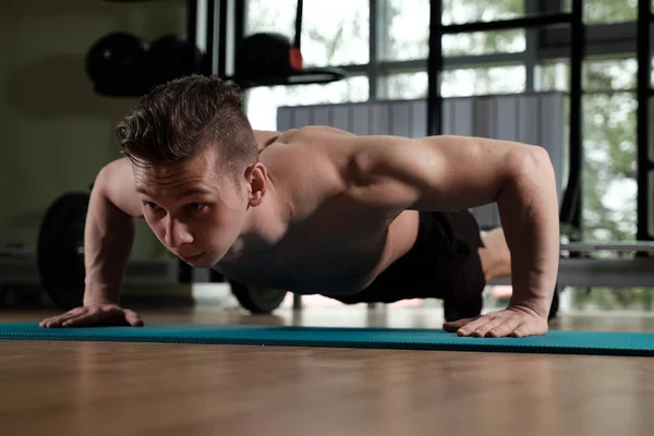 Musculoso chico con un torso desnudo está empujando hacia arriba en el gimnasio . — Foto de Stock