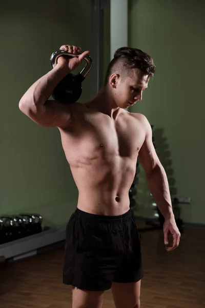 Muskularny facet z Naga tułowia w szorty sportowe trzyma ciężar na ramieniu, kłania głową. — Zdjęcie stockowe